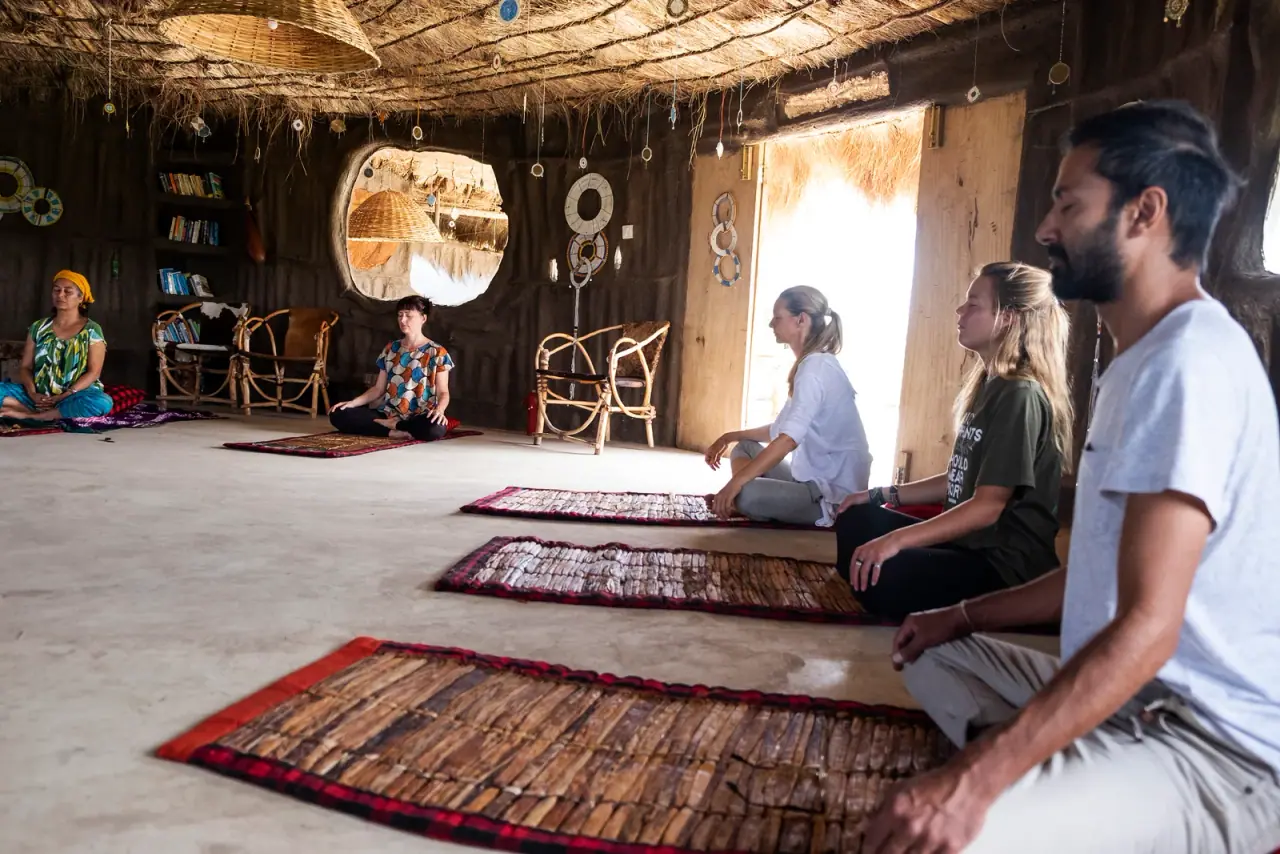 Guests meditating on woven mats inside the thatched yoga and wellness room at Africa Amini Original Maasai Lodge