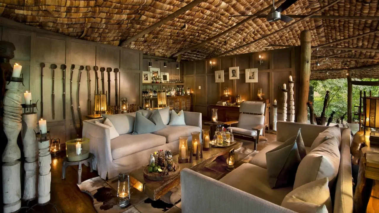 Wood-panelled bar and sitting area decorated with tribal weapons and framed photographs at andBeyond Lake Manyara Tree Lodge