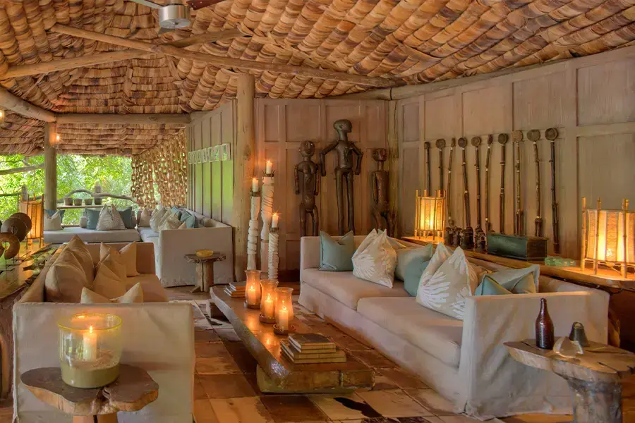 Candlelit lounge at andBeyond Lake Manyara Tree Lodge with carved tribal figures and thatched shingle ceiling