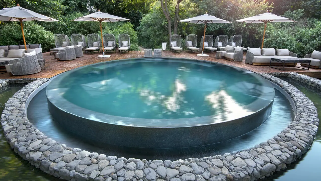Round stone-edged swimming pool set into the groundwater forest canopy at andBeyond Lake Manyara Tree Lodge