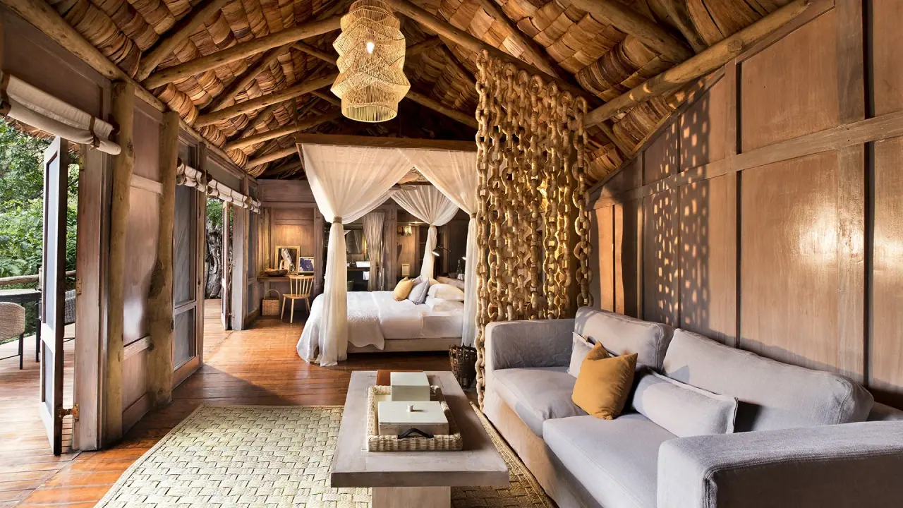 Treehouse suite bedroom with a draped four-poster bed and woven chain room divider at andBeyond Lake Manyara Tree Lodge