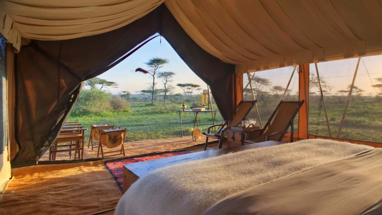 Mobile camp bedroom at andBeyond Serengeti Under Canvas opening onto the open Serengeti grassland at sunrise