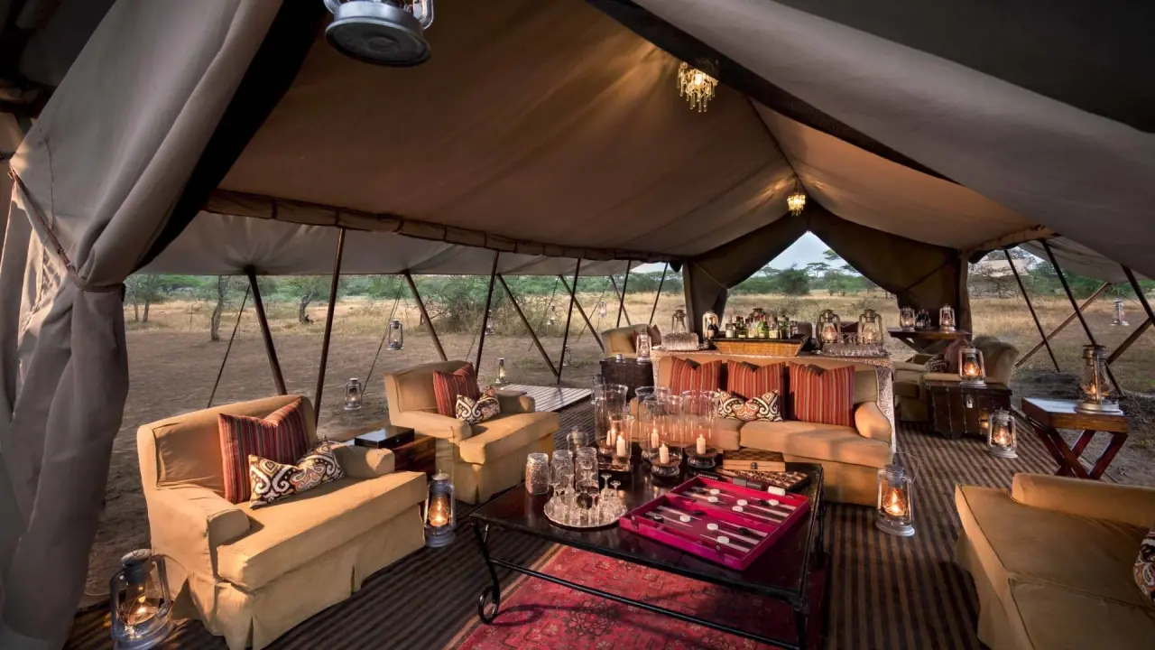 Safari-style lounge tent at andBeyond Serengeti Under Canvas with striped armchairs, a backgammon table and hurricane lanterns
