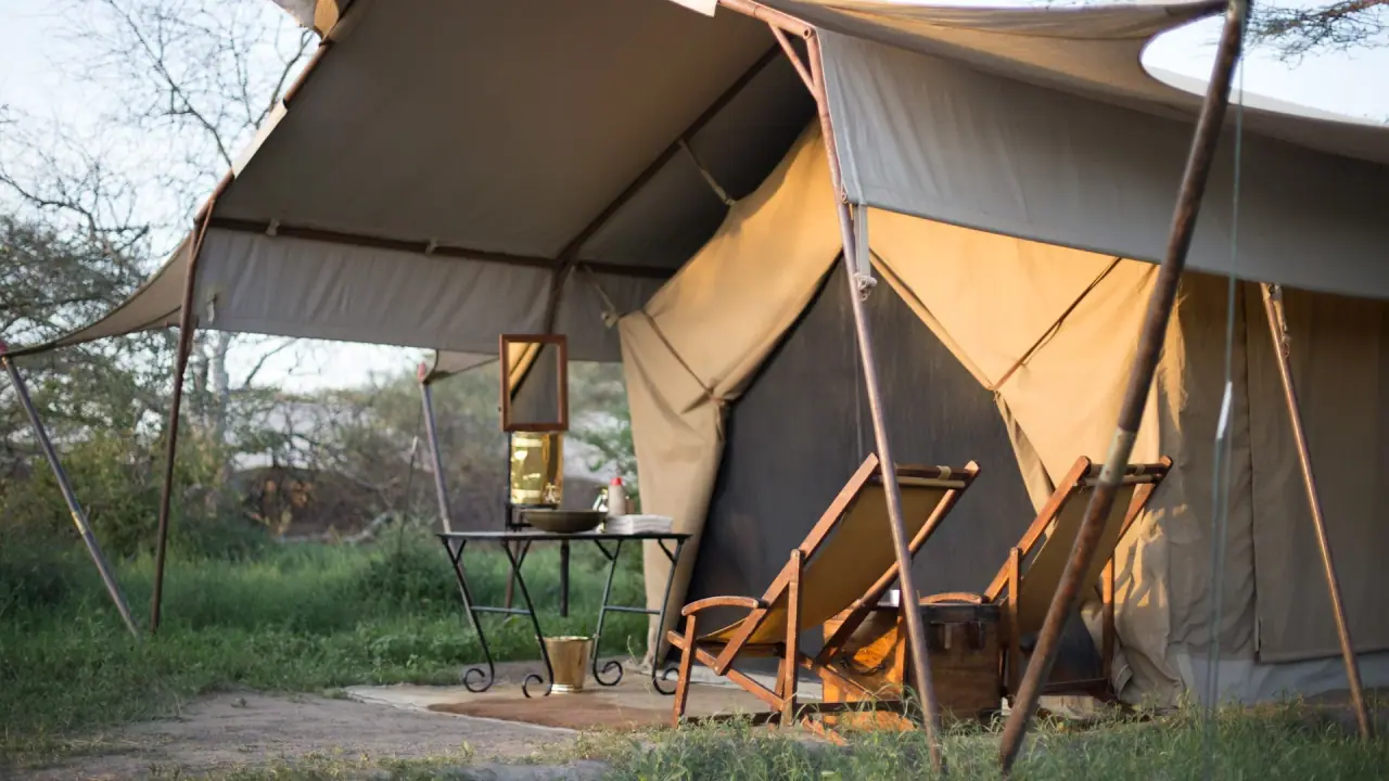 Canvas guest tent veranda at andBeyond Serengeti Under Canvas with camp chairs and a washstand mirror at golden hour