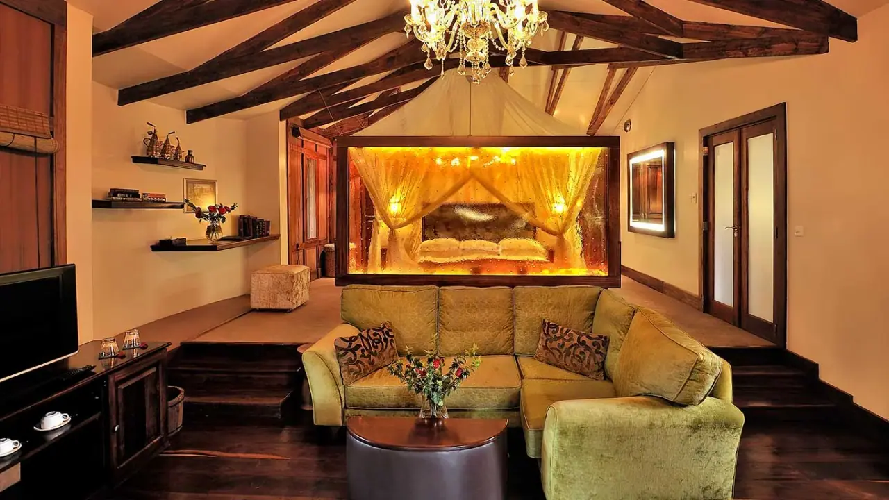 Suite sitting room at Arusha Coffee Lodge with a glowing four-poster bed alcove and chandelier over a green sofa