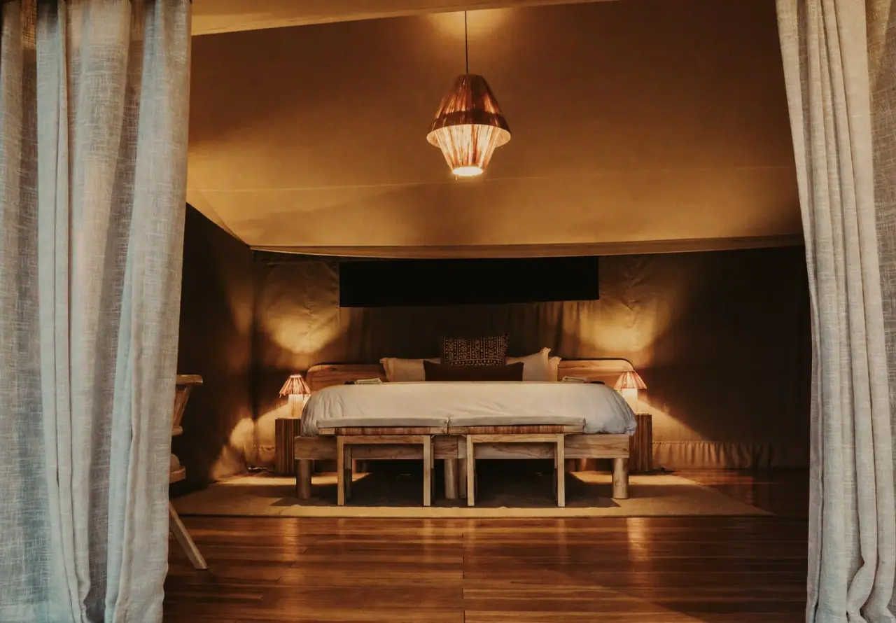 Dimly lit safari tent bedroom at Conserve Safari Tarangire with a king bed and twin bench seating