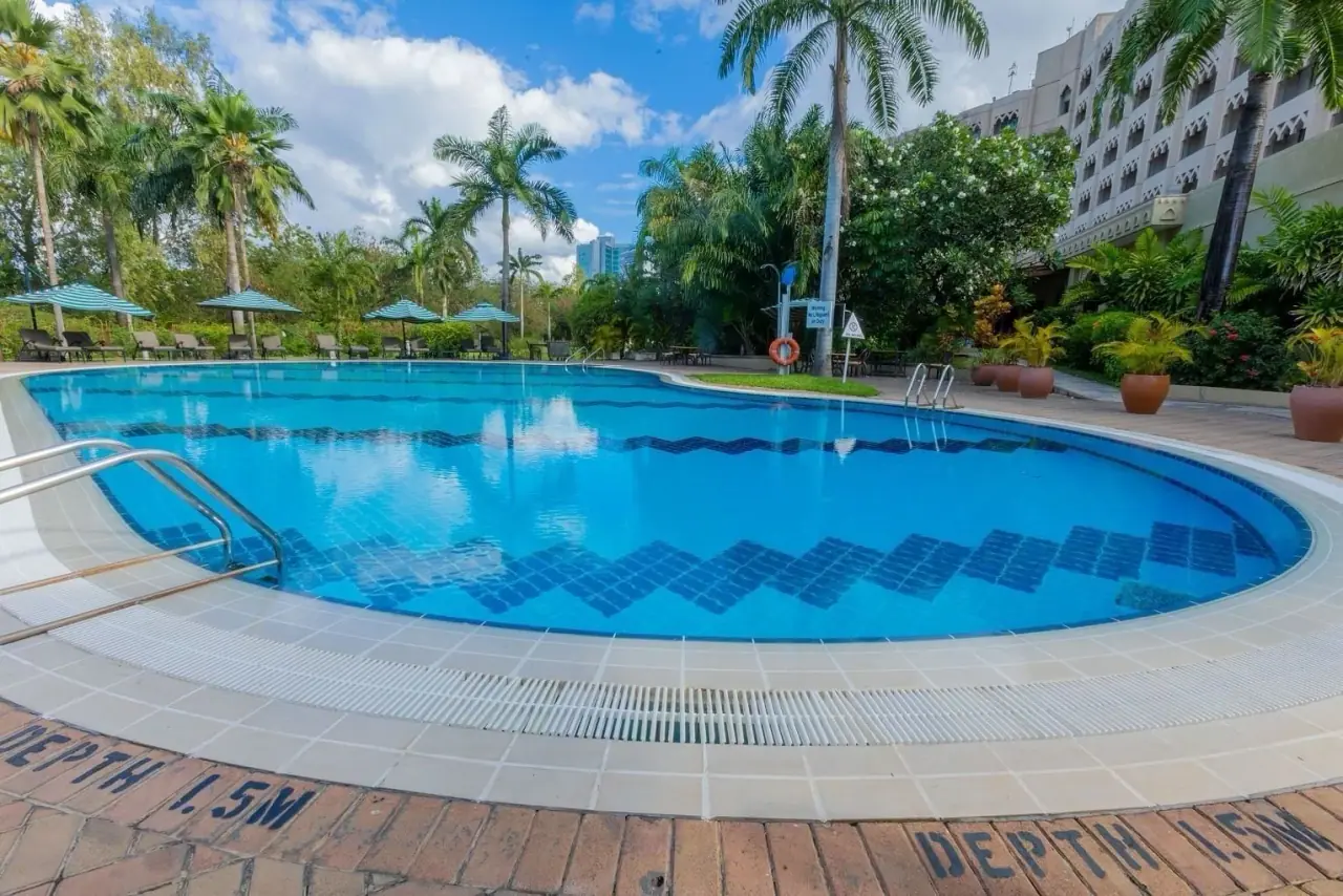 Outdoor swimming pool surrounded by palm trees and striped umbrellas at Dar es Salaam Serena Hotel
