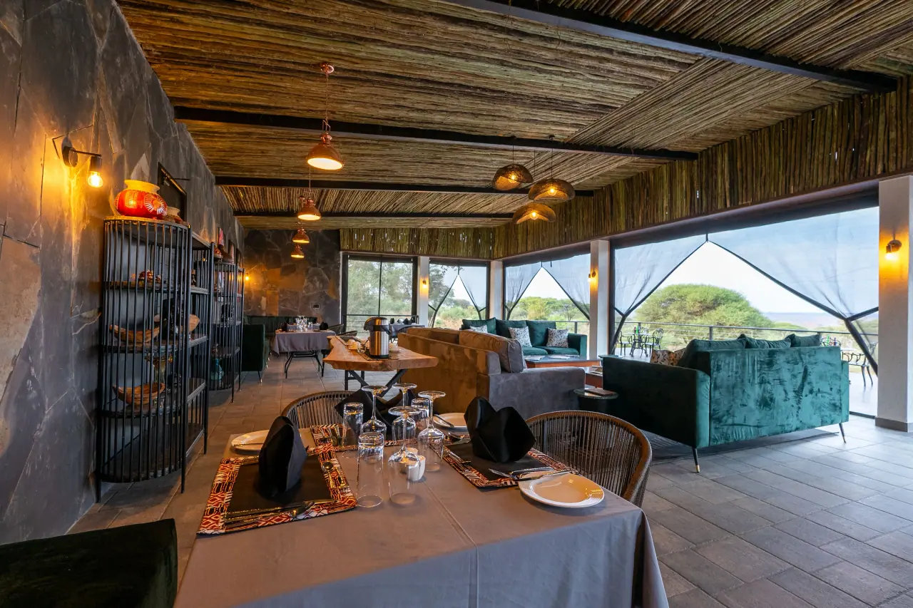 Open-sided lounge and dining area at Elephant Springs with green sofas and a reed ceiling