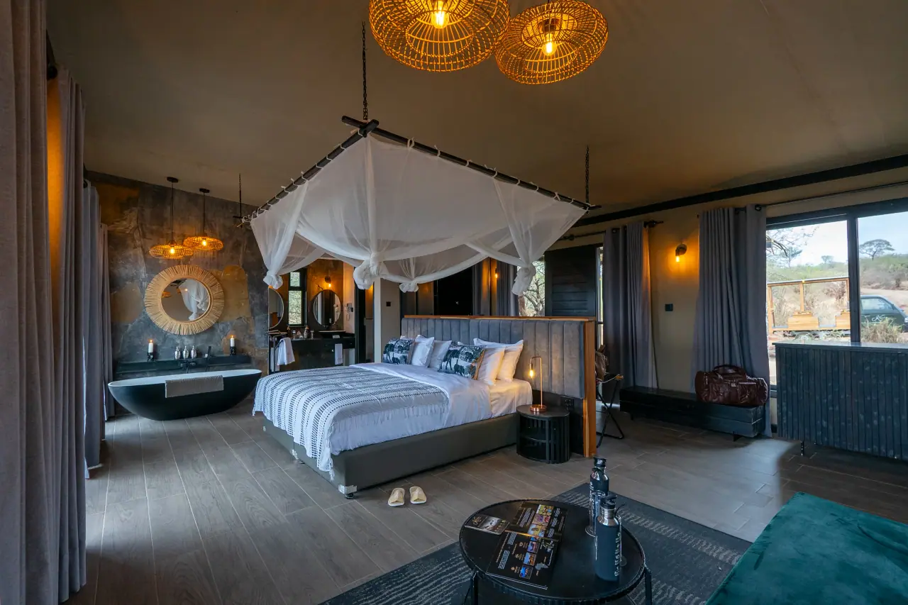 Suite bedroom at Elephant Springs with a canopy-netted bed and freestanding tub beside a stone feature wall