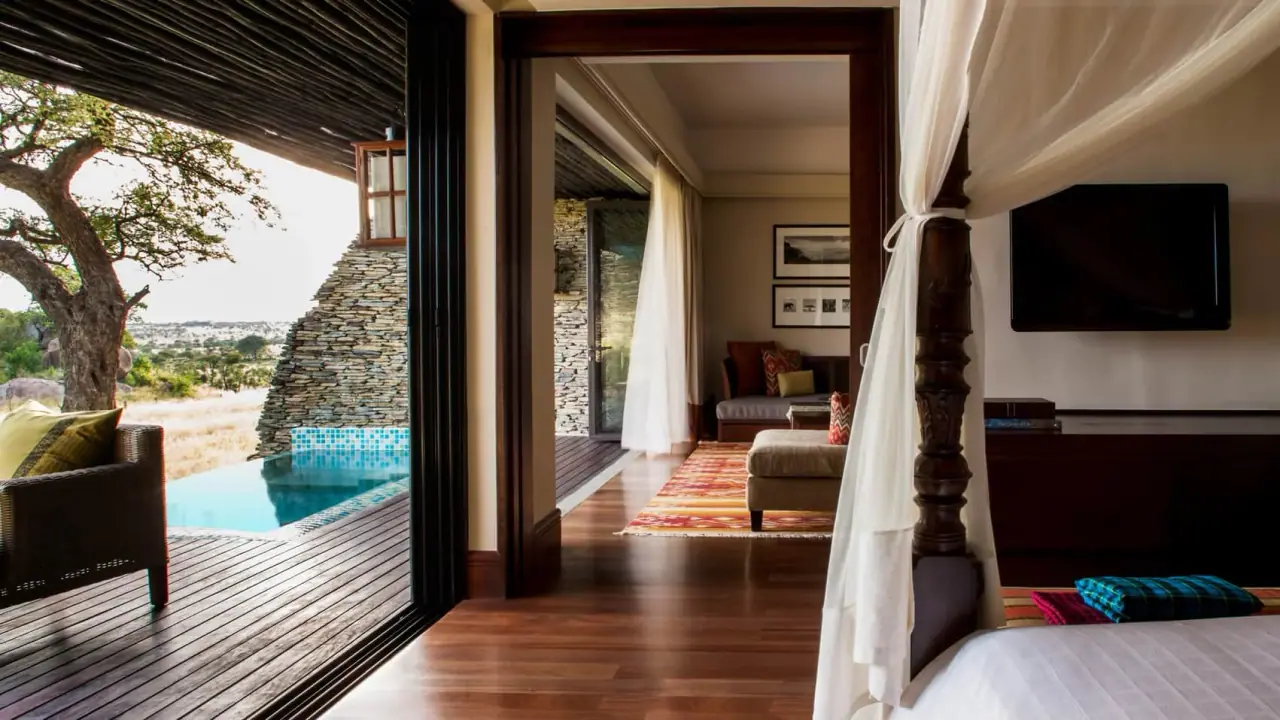 Suite interior with a four-poster bed and pool-view deck at Four Seasons Safari Lodge Serengeti