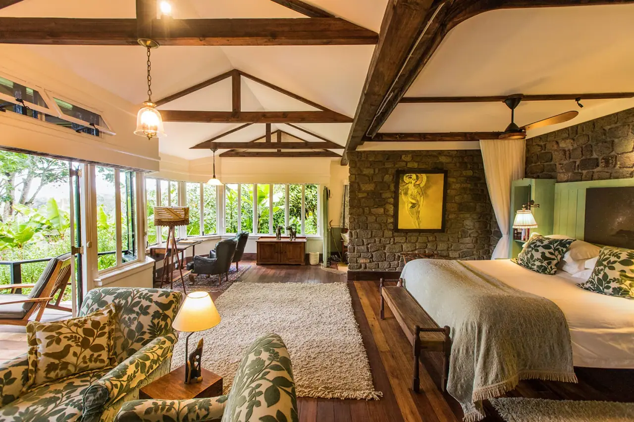 Beamed-ceiling suite bedroom with a stone feature wall and garden-facing sitting area at Gibb's Farm