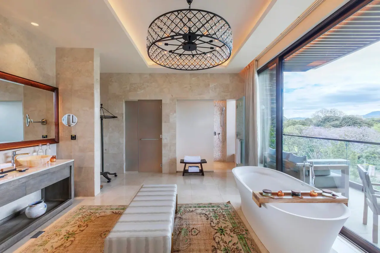 Suite bathroom at Gran Melia Arusha with a freestanding tub, chandelier and private balcony overlooking the grounds