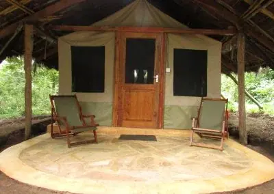 Tent entrance and porch with camp chairs on a circular stone patio at Hondo Hondo Udzungwa Forest Camp