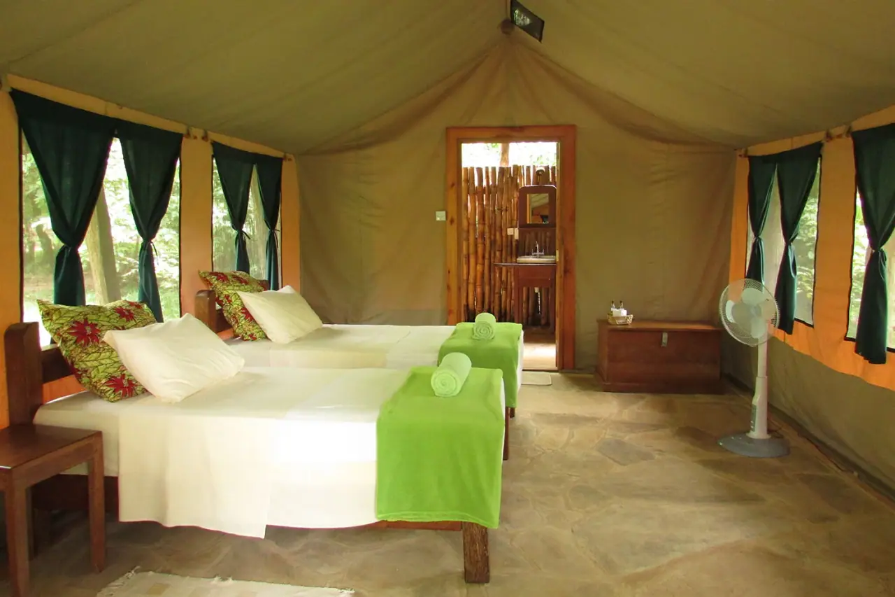 Twin-bed tent interior at Hondo Hondo Udzungwa Forest Camp with green throws and an en-suite bamboo bathroom