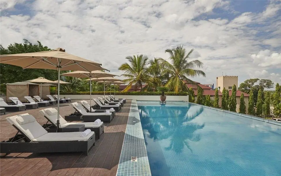Daytime view of the rooftop pool deck and sun loungers at Hyatt Regency Dar es Salaam with coconut palms and city rooftops beyond