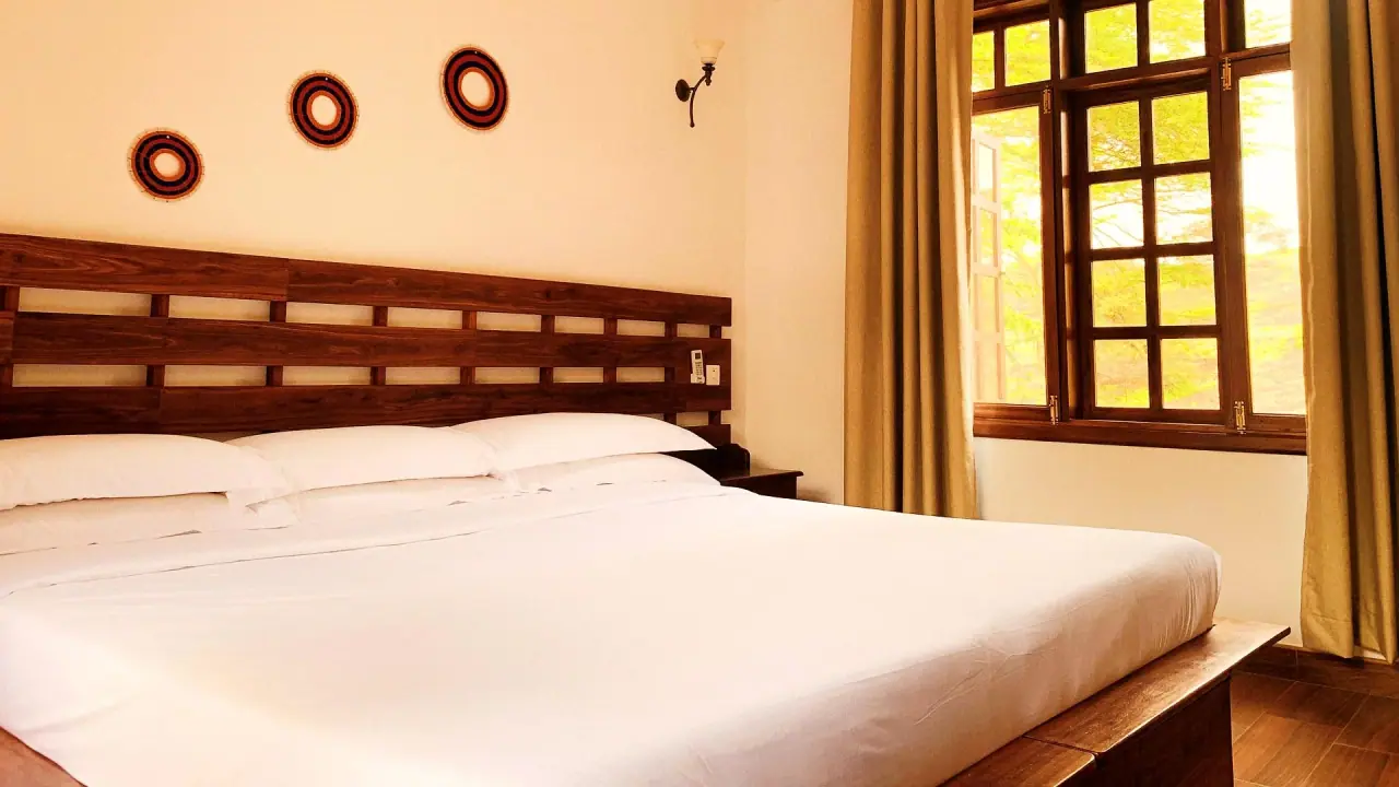 Guest bedroom at Kahawa House with a wooden headboard and window overlooking the coffee estate greenery