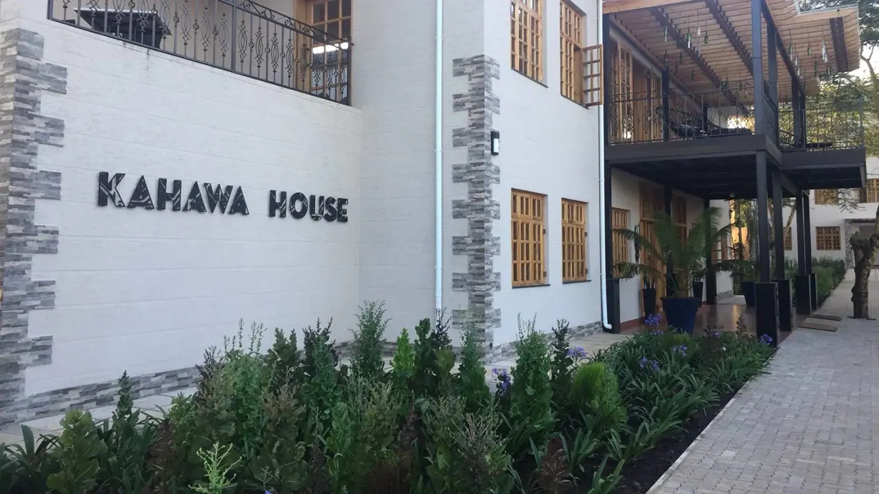 Kahawa House entrance wall signage beside stone-clad pillars and a flower-lined walkway