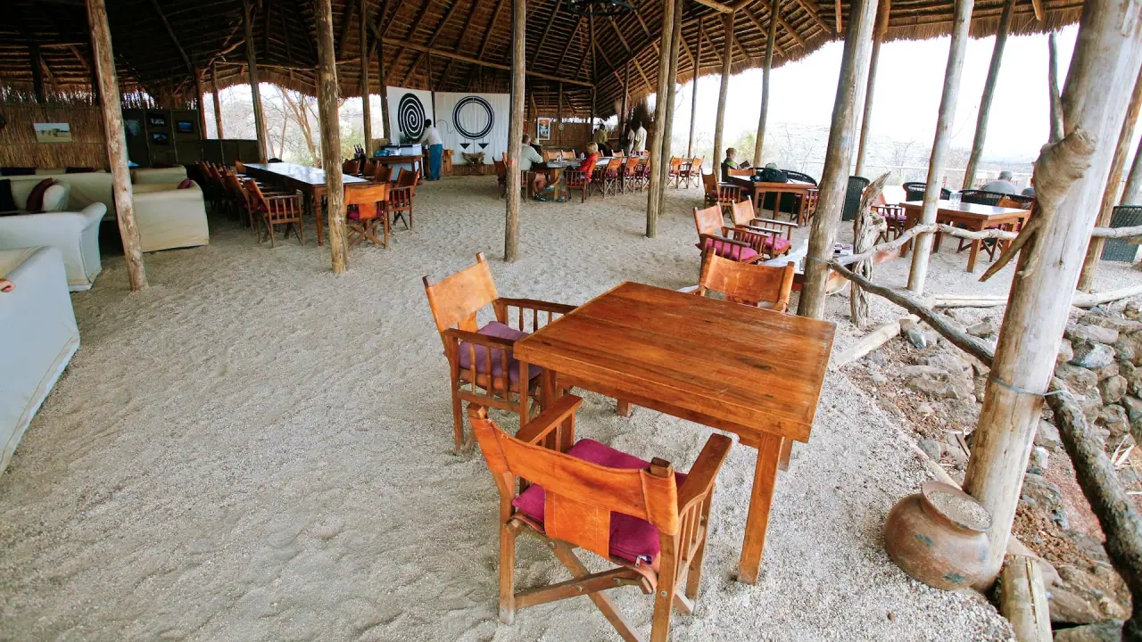 Open-sided thatched dining and lounge area at Kambi ya Tembo with sand floor and safari-style furniture