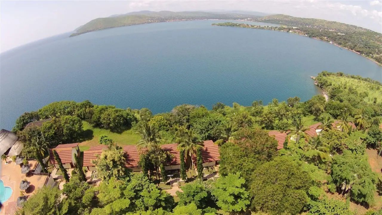 Aerial view of Kigoma Hilltop's red-roofed cottages set among trees above the bay of Lake Tanganyika