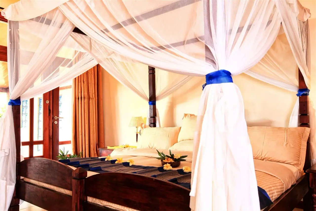 Canopy bed guest room at Kigoma Hilltop draped in sheer mosquito netting with a blue ribbon accent