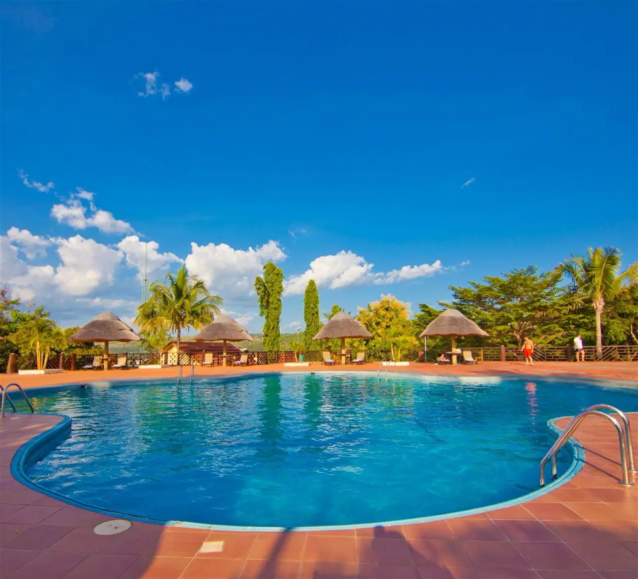 Round swimming pool at Kigoma Hilltop surrounded by thatched sun shelters and palm trees