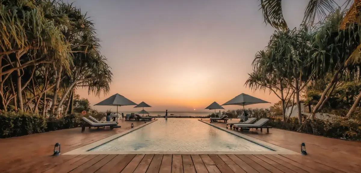 Infinity pool at Kilindi Zanzibar framed by palm trees facing the Indian Ocean at sunset