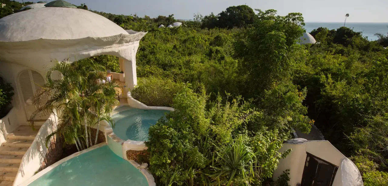 Aerial view of a domed Kilindi Zanzibar pavilion with cascading private pools set into the forested hillside above the ocean