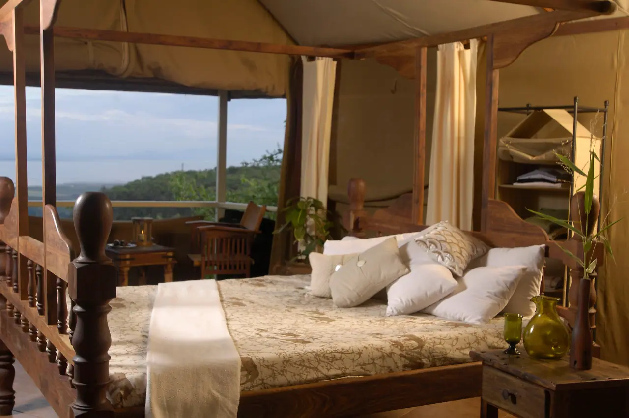 Four-poster suite bed at Kirurumu Manyara Lodge with sheer curtains and a distant view of Lake Manyara