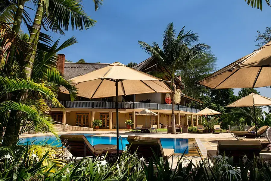 Swimming pool and thatched main house framed by palm trees at Kitela Lodge near Karatu