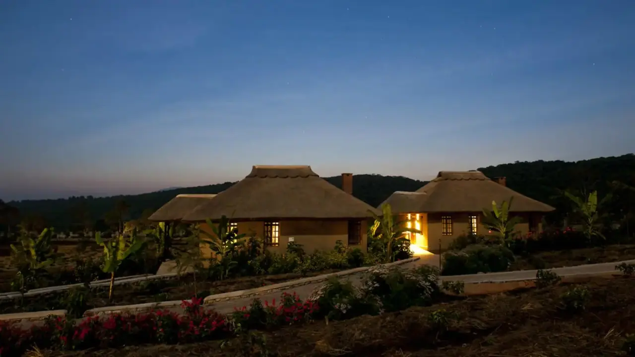 Thatched guest cottages glowing with interior light at dusk at Kitela Lodge