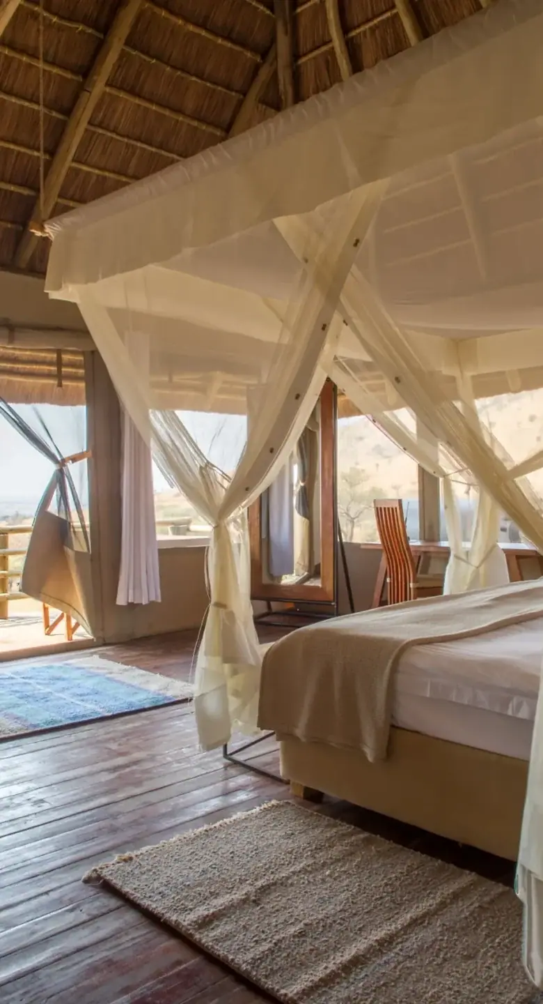 Canvas guest tent at Kubukubu Tented Lodge with a mosquito-net canopy bed and open view of the plains