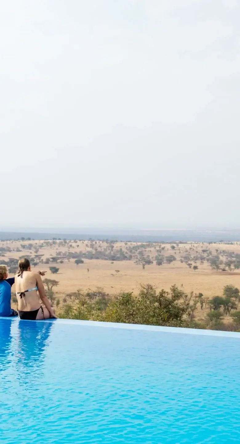 Guests relaxing at the edge of the infinity pool overlooking the Serengeti plains at Kubukubu Tented Lodge