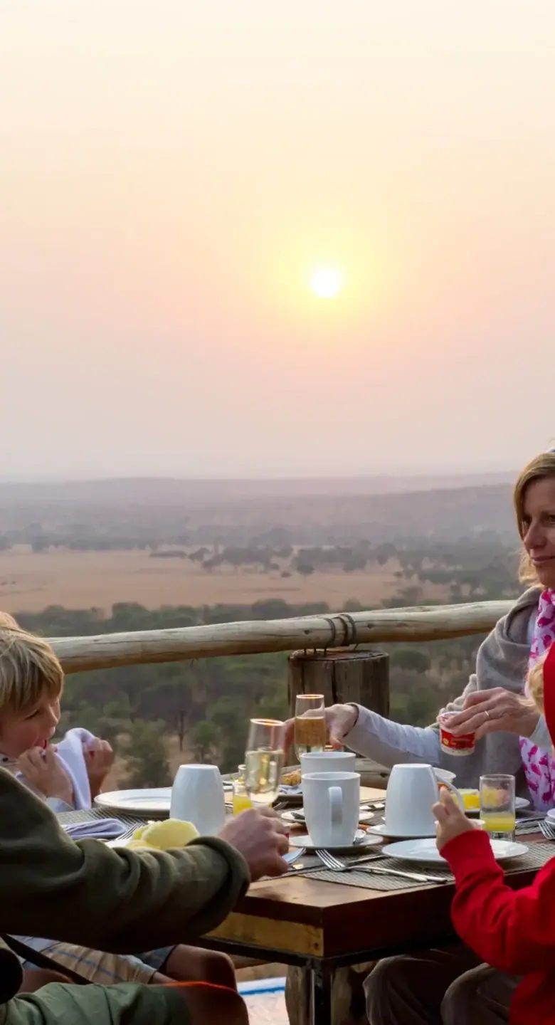 Family enjoying breakfast on the deck at sunset overlooking the Serengeti plains at Kubukubu Tented Lodge