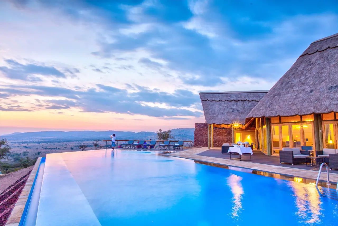 Infinity pool at dusk beside the thatched main lodge at Lahia Tented Lodge overlooking the central Serengeti plains