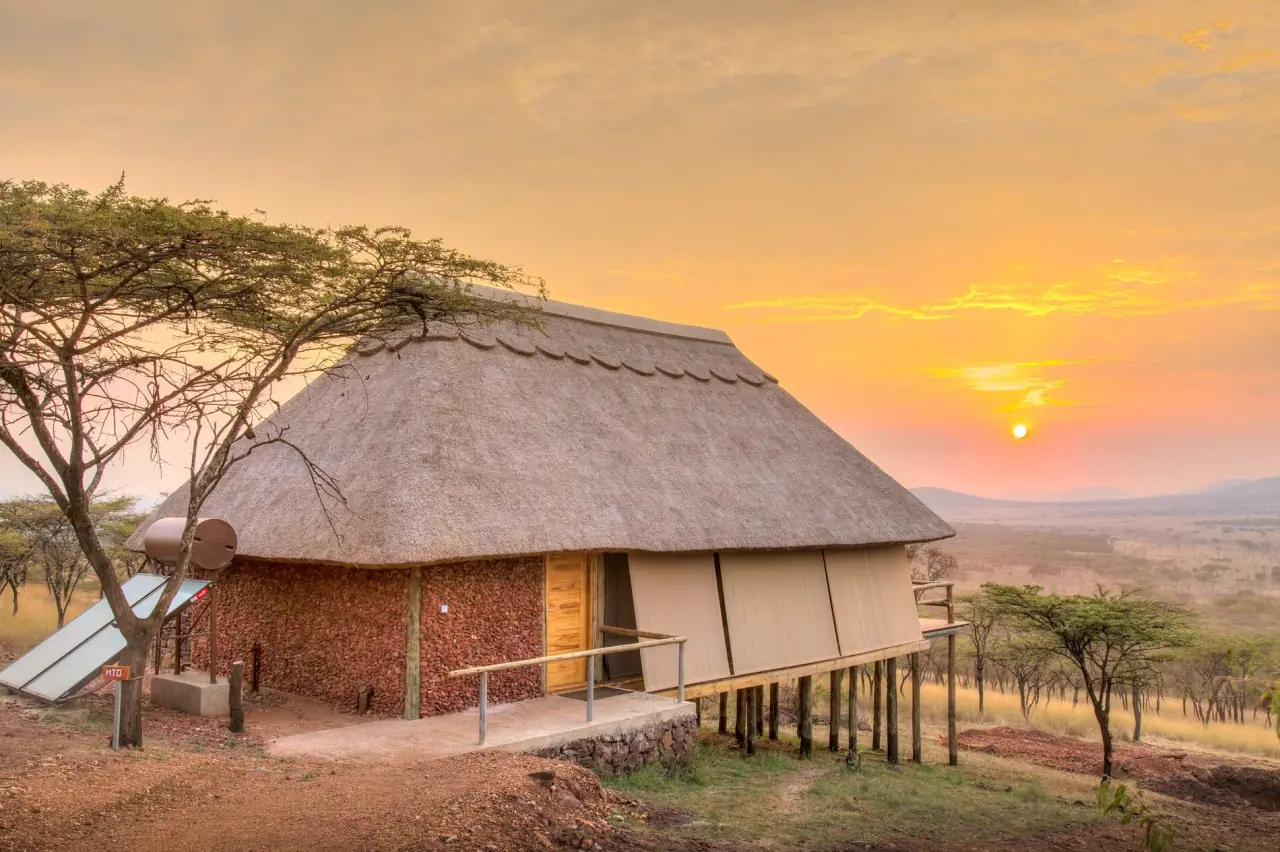 Stilted guest tent with thatched roof at Lahia Tented Lodge at sunrise over the Serengeti