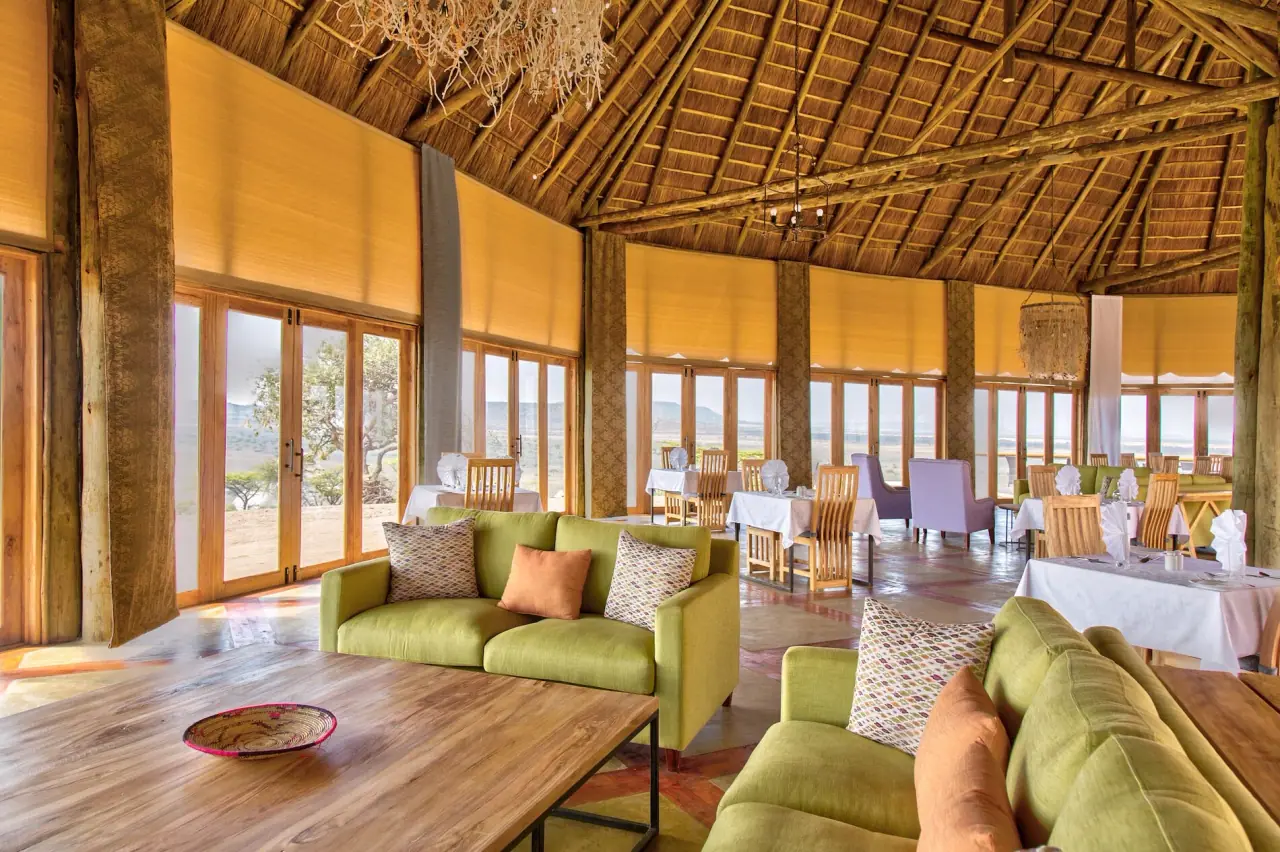Thatched lounge and dining area at Lahia Tented Lodge with green sofas and panoramic plains views