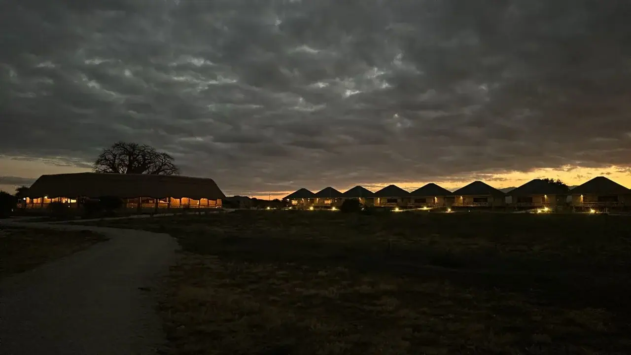 Row of guest tents lit up at dusk under a dramatic cloudy sky at Lake Burunge Baobab Tented Lodge