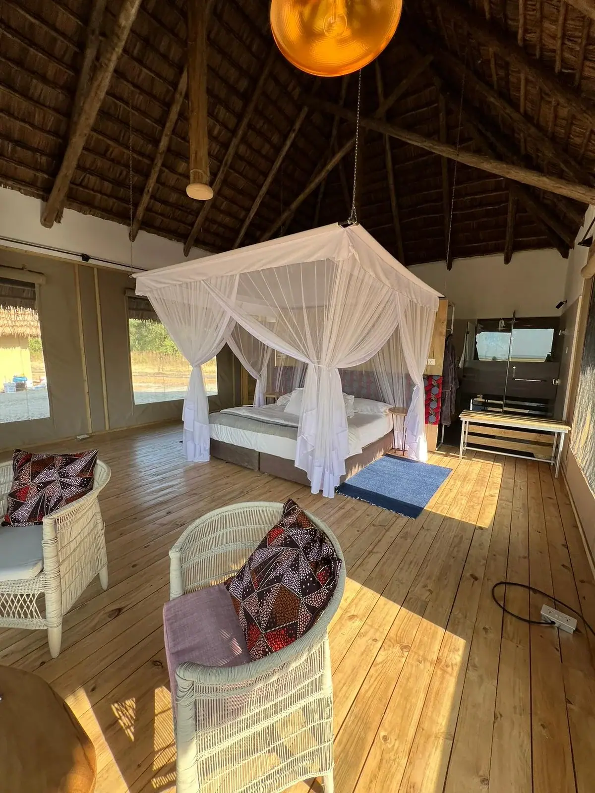 Tented guest room at Lake Burunge Baobab Tented Lodge with a white canopy bed and wicker armchairs