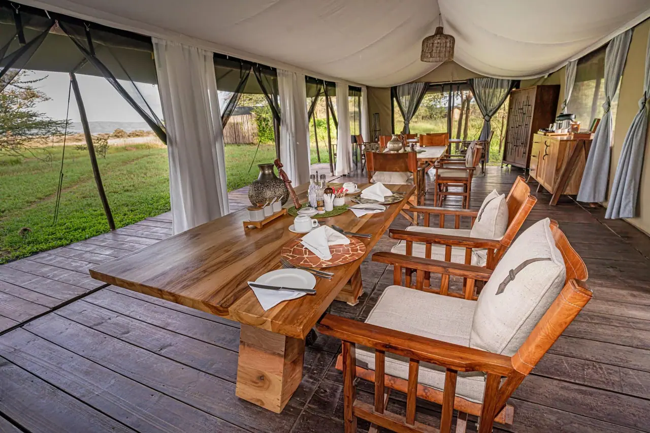 Tent interior with a wooden dining table and chairs opening onto the plains