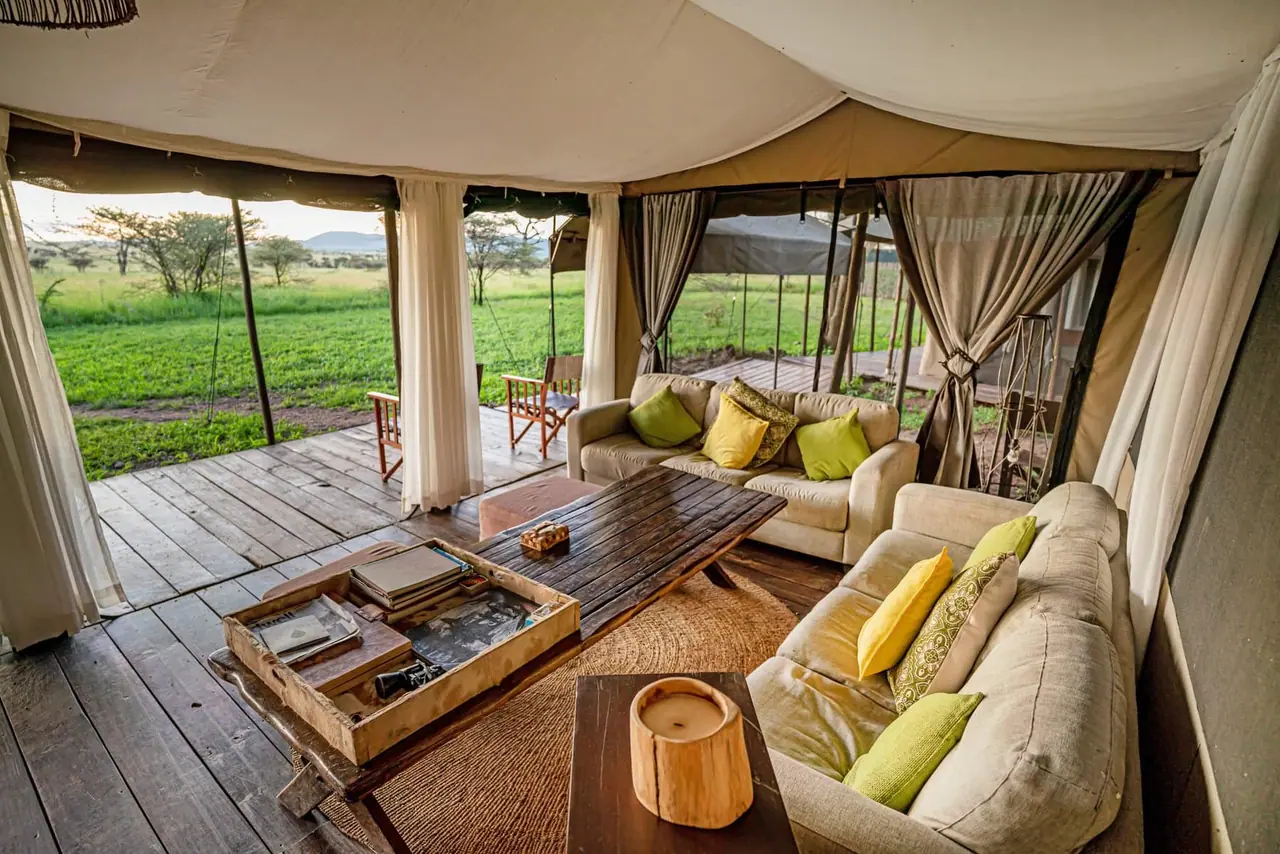 A tent lounge with sofas and a view of the grassland through open flaps