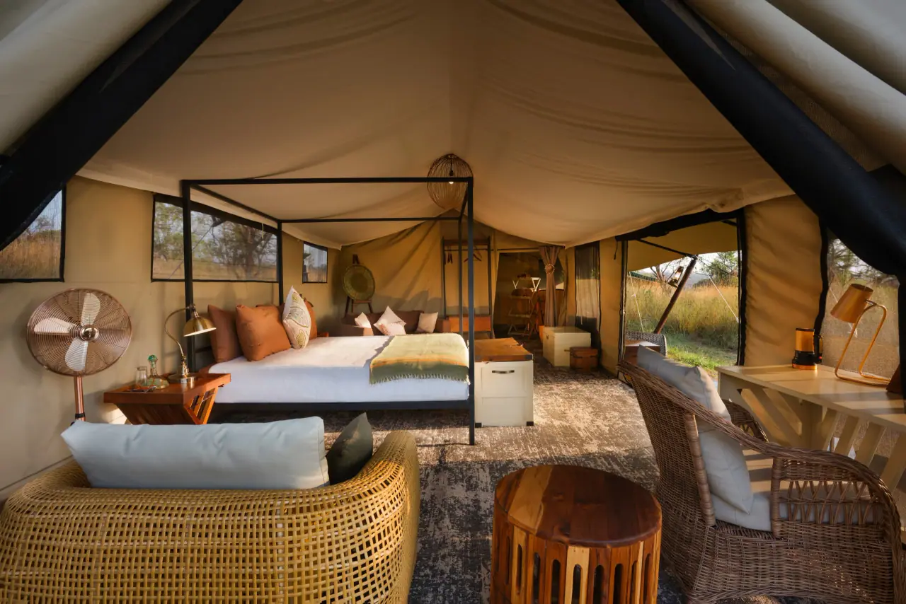 A guest tent with a bed, wicker chairs and a wide view of the savannah