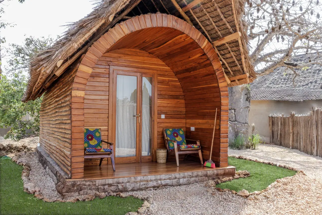 Arched thatched-roof guest cottage at Makofi Guest House with a private veranda and two patterned armchairs, Zanzibar Island