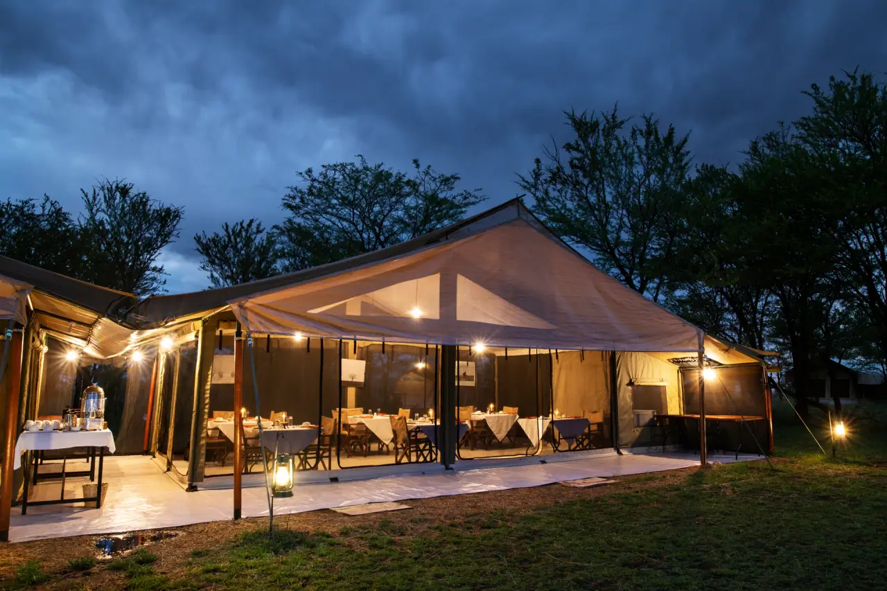 Mara Katikati Tented Camp's dining tent lit up at dusk with lanterns and set tables, northern Serengeti