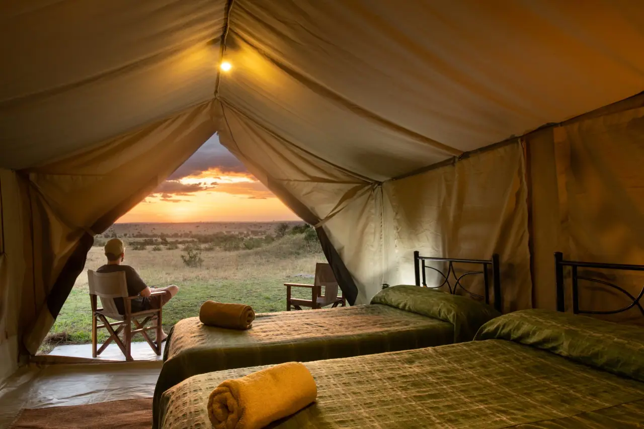 Guest relaxing on the deck of a twin-bed tent at Mara Katikati Tented Camp, watching the Serengeti sunset