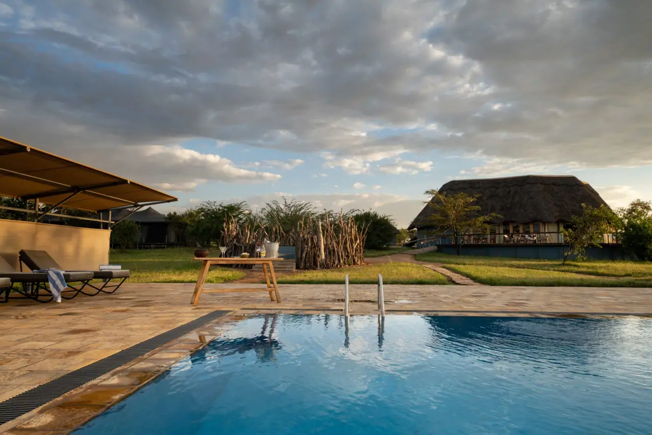 Swimming pool and stone sundeck at Mara Mara Tented Lodge with the thatched main lodge in the background