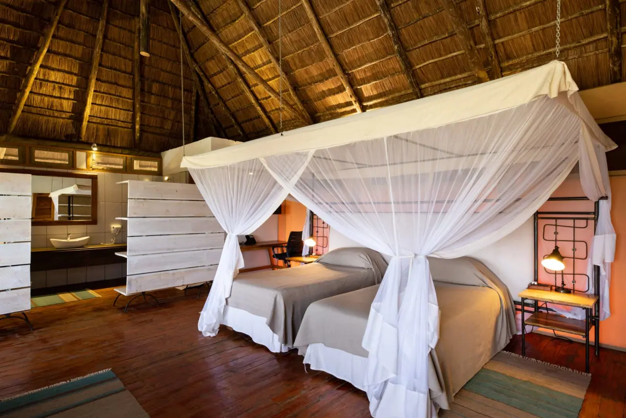 Thatched-roof suite at Mara Mara Tented Lodge with twin beds under a mosquito net and an en-suite dressing area