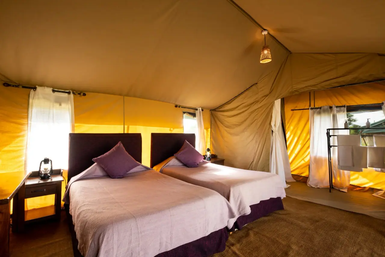 Twin beds with hurricane lanterns inside a guest tent at Mara Under Canvas