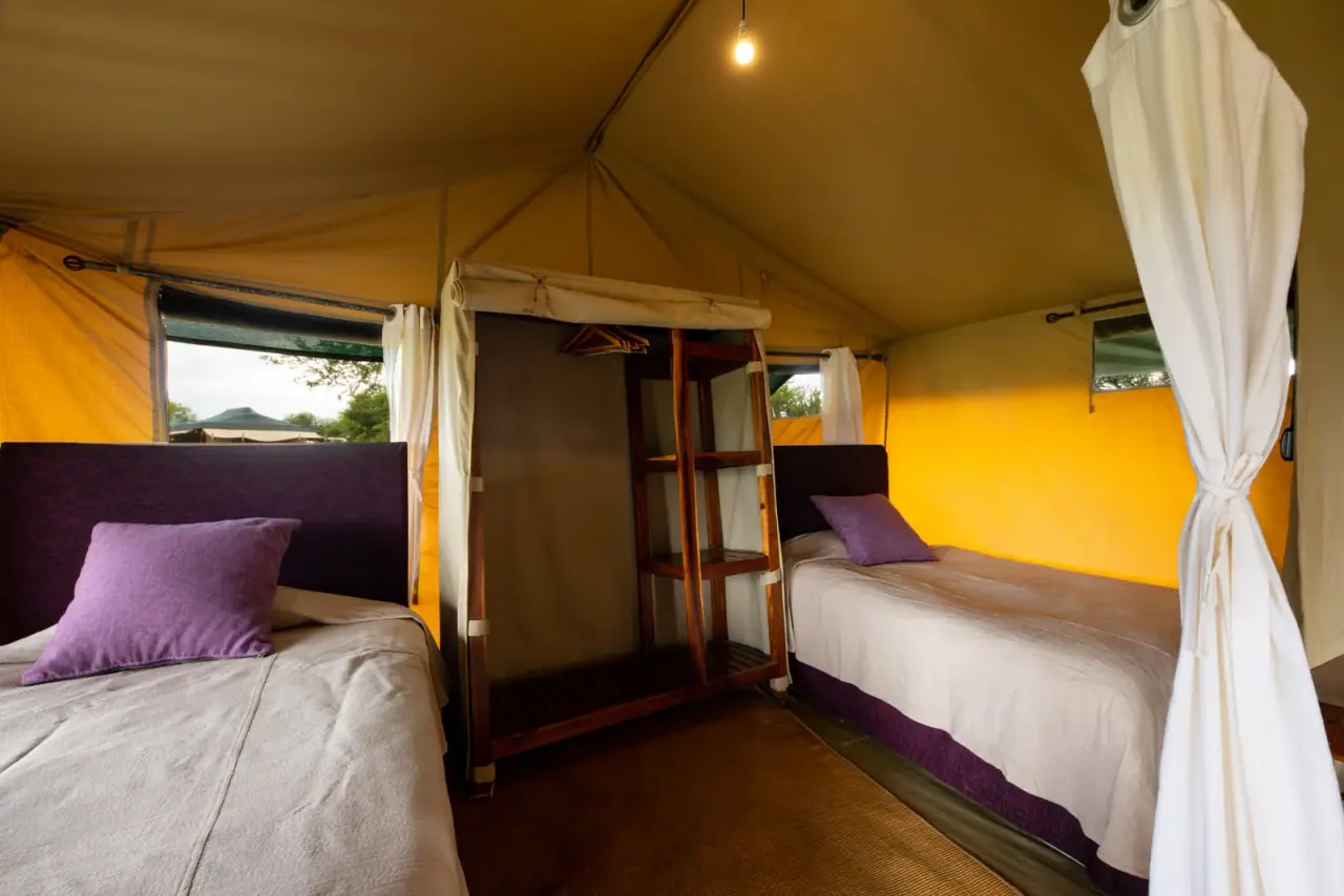 Twin beds and canvas wardrobe inside a guest tent at Mara Under Canvas