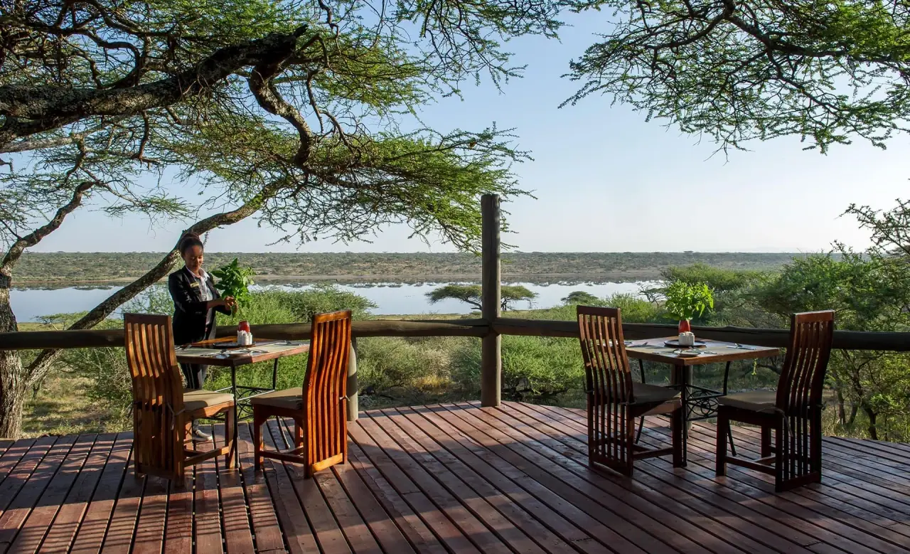 Staff member setting a private dining table on the deck at Masek Tented Lodge overlooking Lake Masek