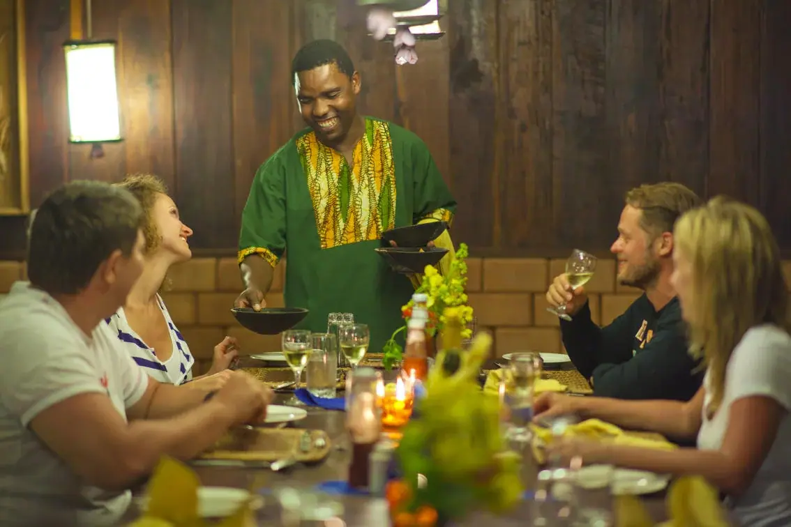 Waiter serving guests in the wood-panelled dining room at Mbali Mbali Gombe Tented Camp